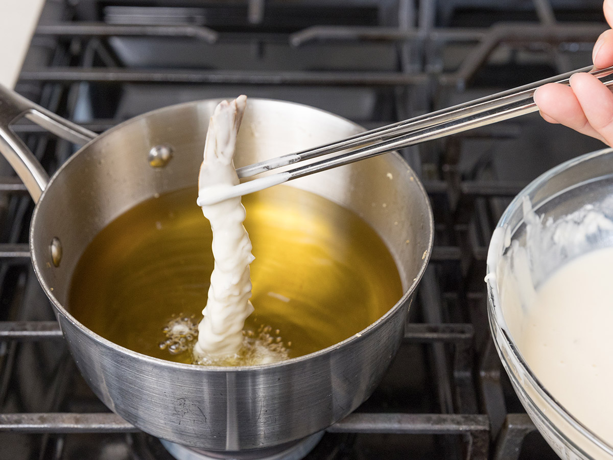 Slowly dropping the batter ebi tempura into hot oil.