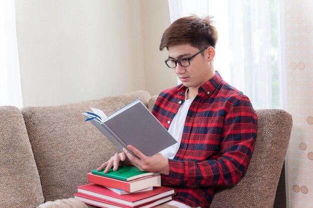Young man wearing eyeglasses sitting on couch, He smile with joyful and looking to a book in hand