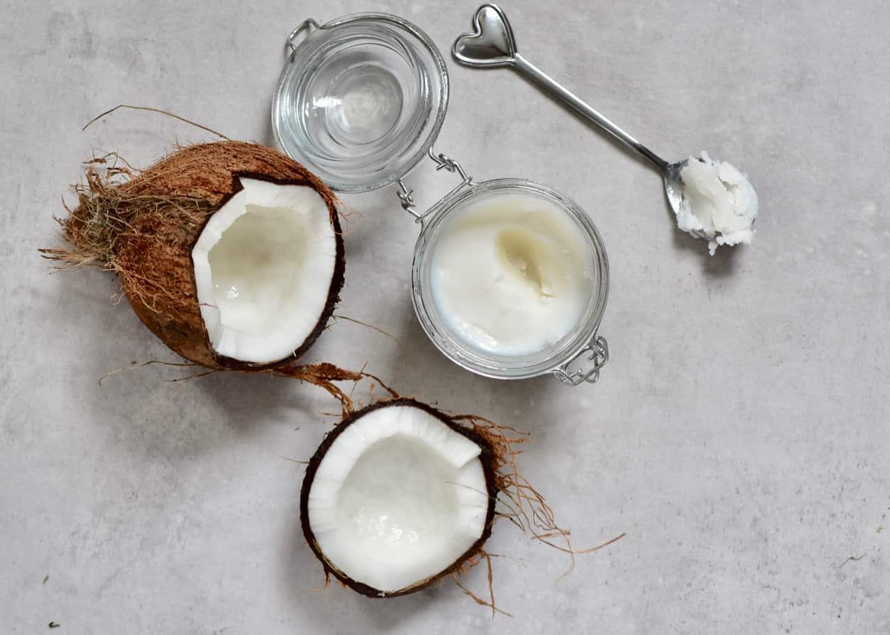 A coconut with a spoon and a jar of coconut oil  Description automatically generated