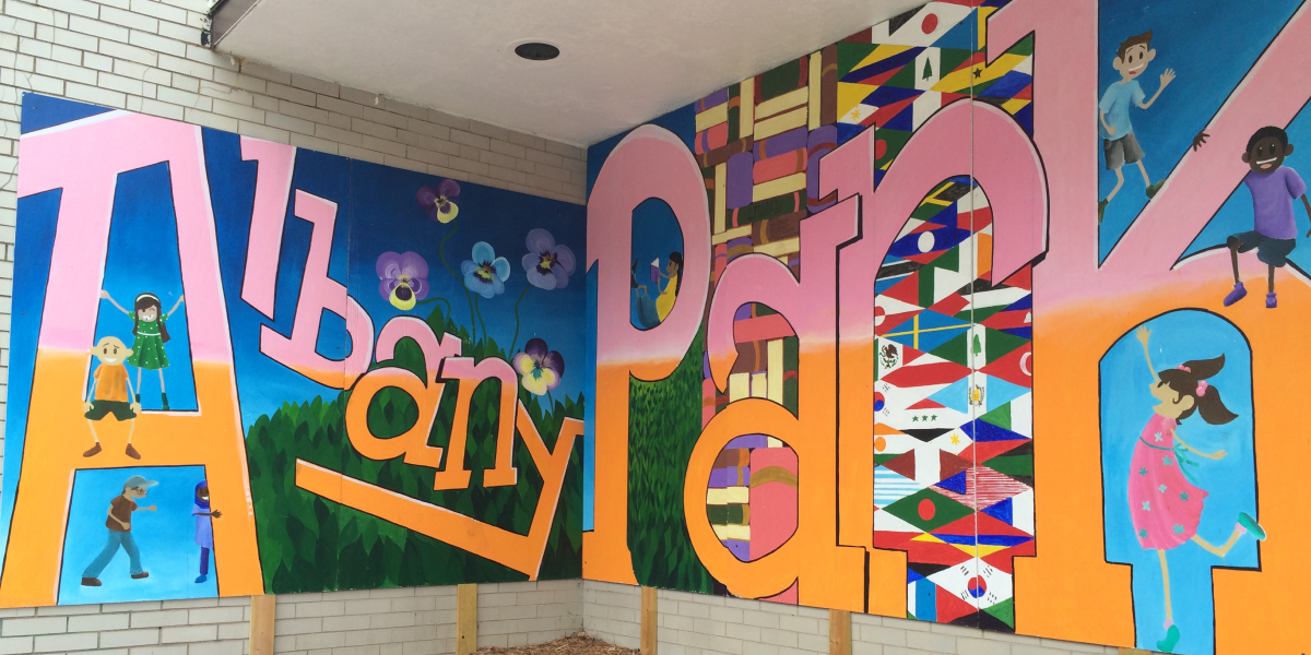 Mural with the words "Albany Park" surrounded by diverse children, flowers, bushes, books, and flags.