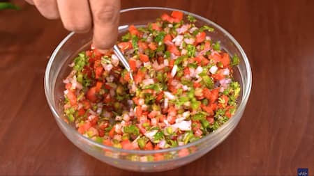Finely chopped onions, capsicum, tomatoes, coriander, and green chilies in a bowl for sandwich filling.