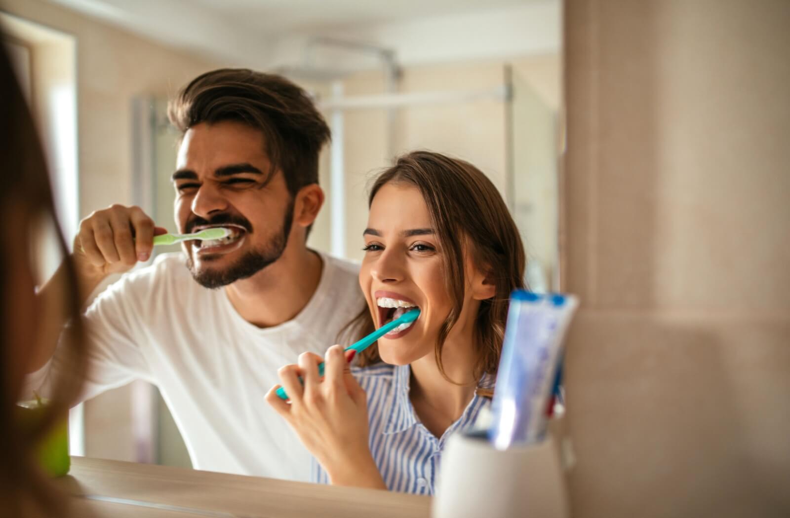 A young couple brushing their teeth together in front of a bathroom mirror.
