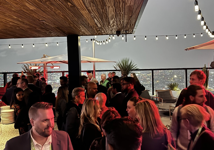 Light-it’s side-event attendees smiling in engaging conversations with LA's illuminated cityscape in the background.