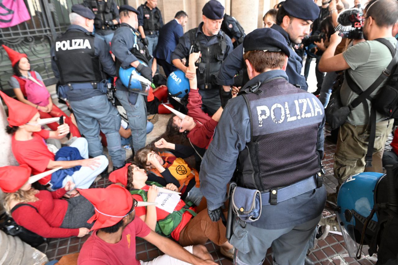 rebels with Pinocchio noses are swamped by police as they sit in an entrance way