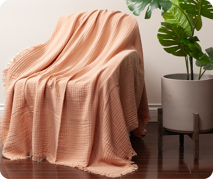 Our Muslin Gauze Throw in Clay shown styled on an armchair.