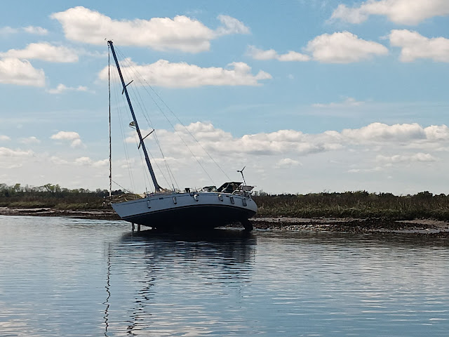 A sailboat that is hard aground.  It is balances on its keel and slumping to one side.  The water is about 6 feet below the waterline of the boat.