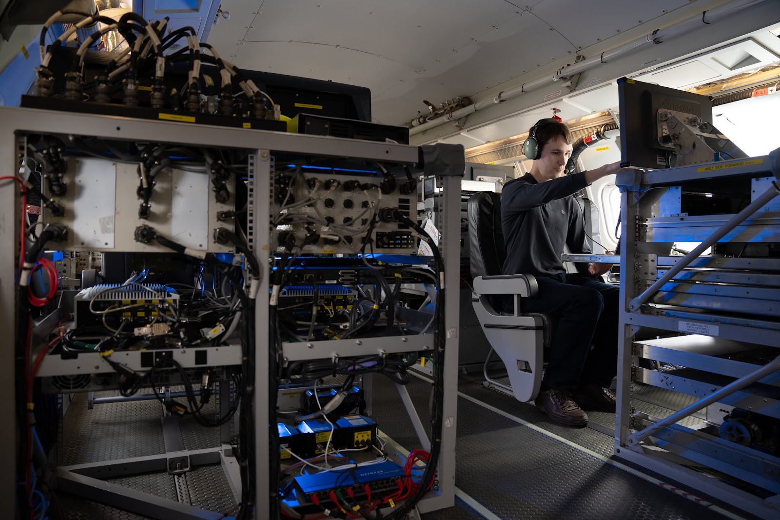 One person sat inside a research aircraft. The person is pointing at a computer screen.