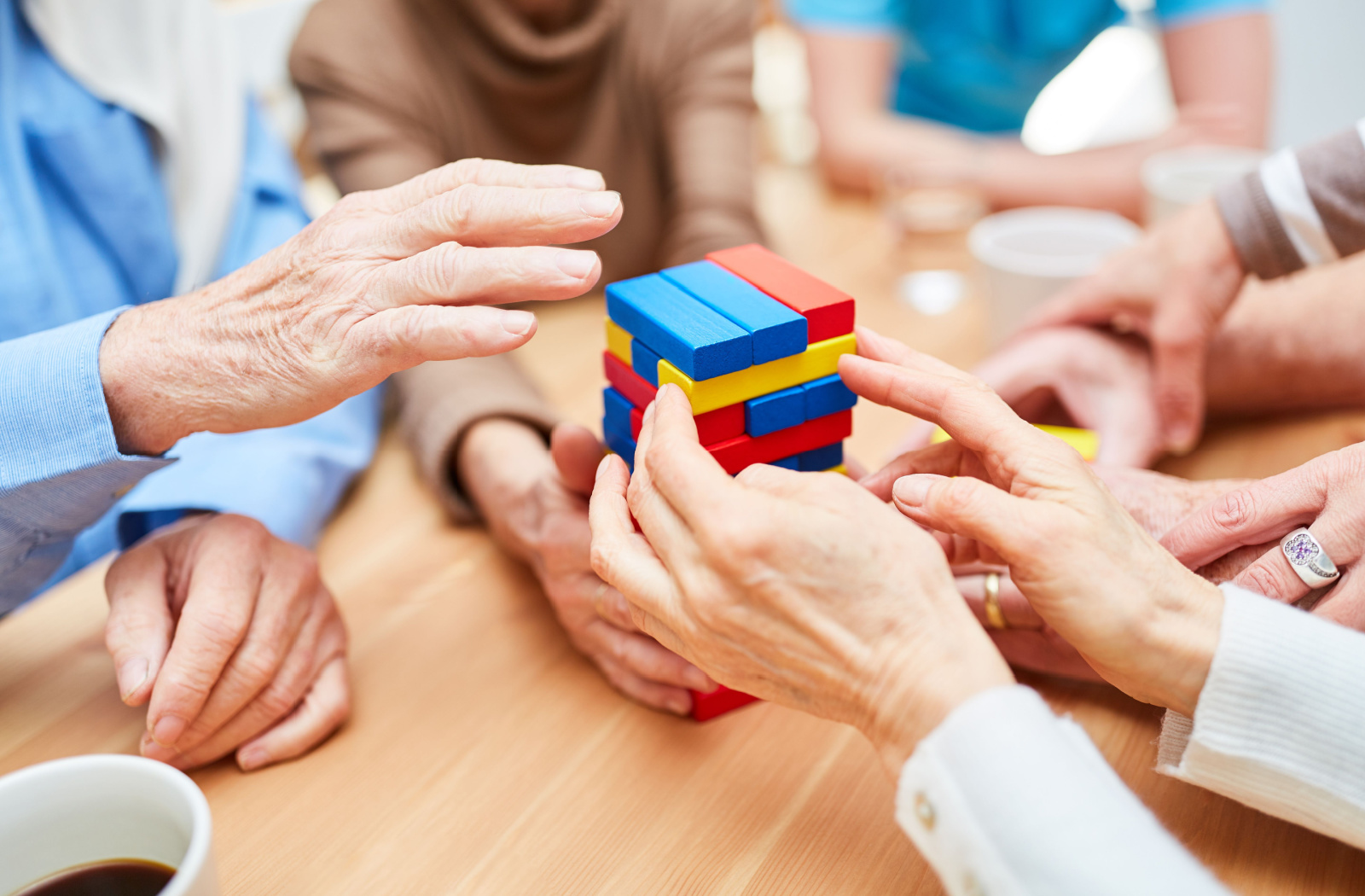 Image of a group of seniors' hands playing with coloured Jenga blocks.