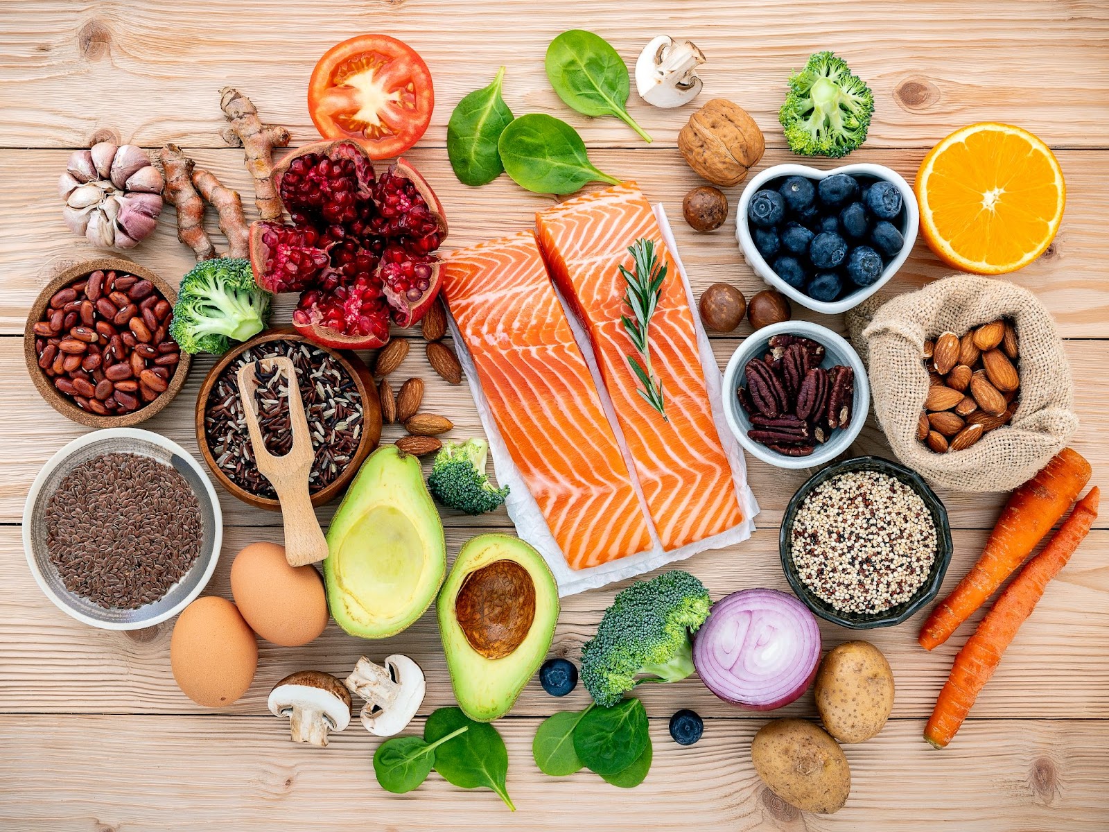 a variety of healthy food salmon, avacado, carrots,eggs,garlic,nuts,blueberry,mushrooms,turmeric, brocoli and orange