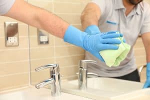 Cleaning worker wiping mirror in a tiled bathroom