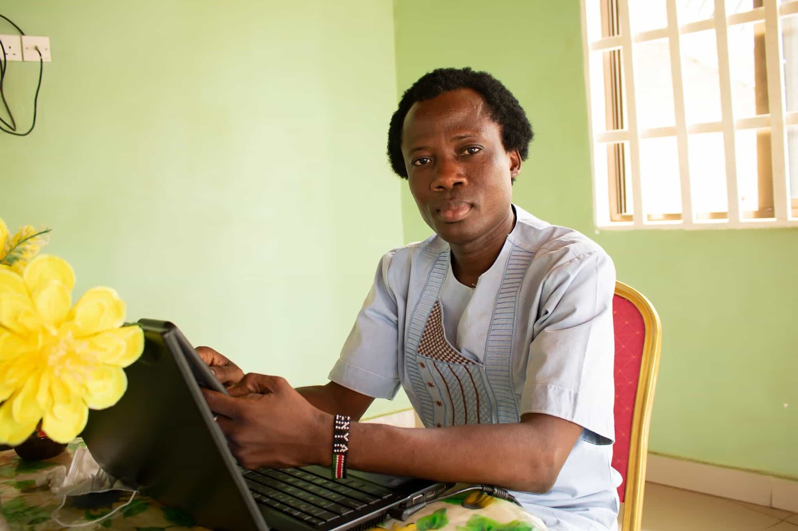 Alhassan Sesay looks to camera while sat at a desk, laptop open.