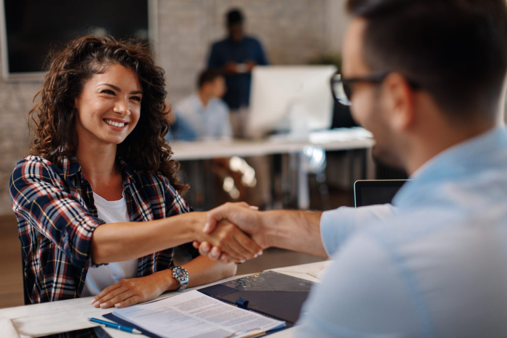 A woman and a man shake hands at a desk, symbolizing a professional interaction. Gain insights by gathering direct user feedback to identify pain points.