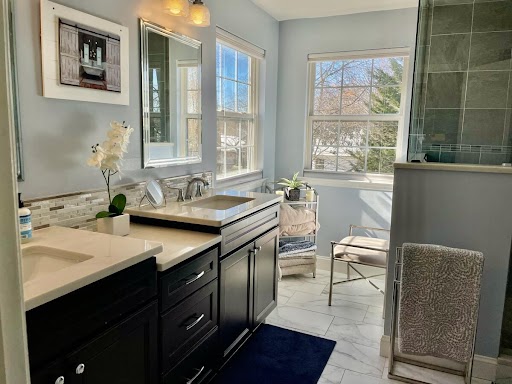 A bathroom with natural light coming in through two windows. The bathroom has a his and hers sink with white countertops and dark cabinetry.