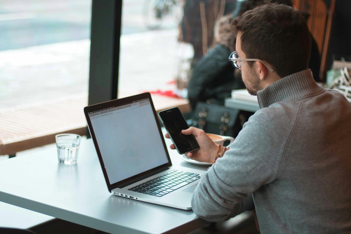 A man using his phone and laptop, searching for an ex-marine motivational speaker for their company event.