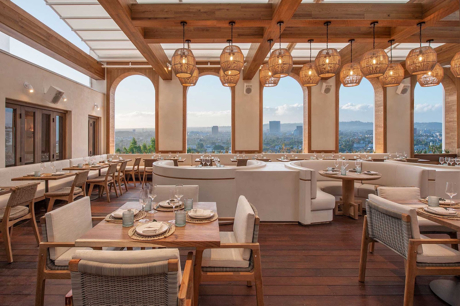 Interior of a restaurant with white-and-wood furniture and large, arched windows looking out over Los Angeles. Casa Madera, West Hollywood, California.