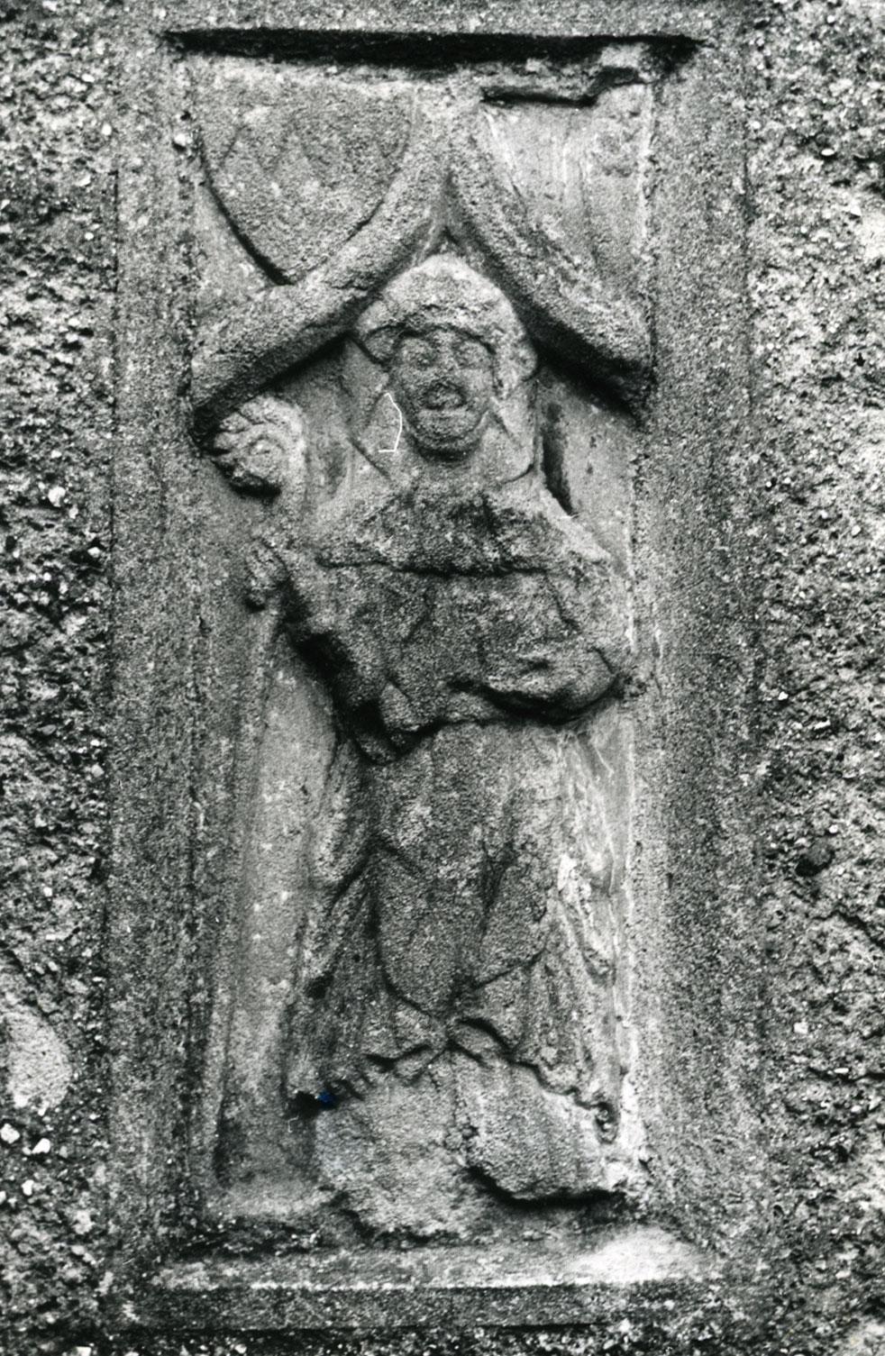 A stone carving of a person holding a cross

Description automatically generated