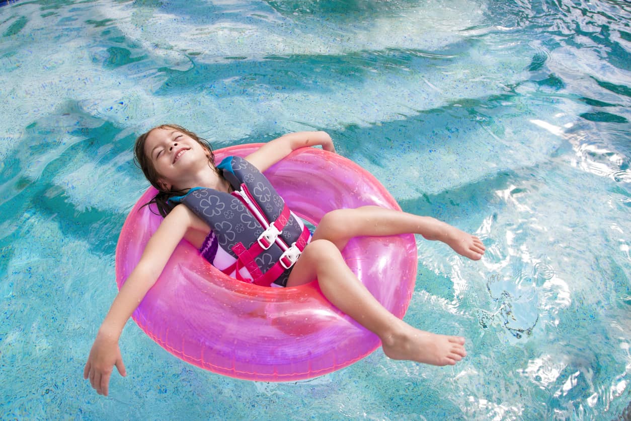 A young child smiles while floating in a pool, wearing a life jacket to ensure safety.