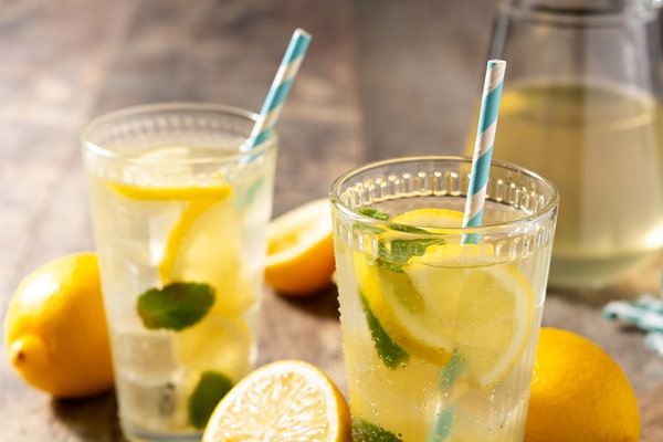 Glasses of lemon juice with a straw surrounded by lemons