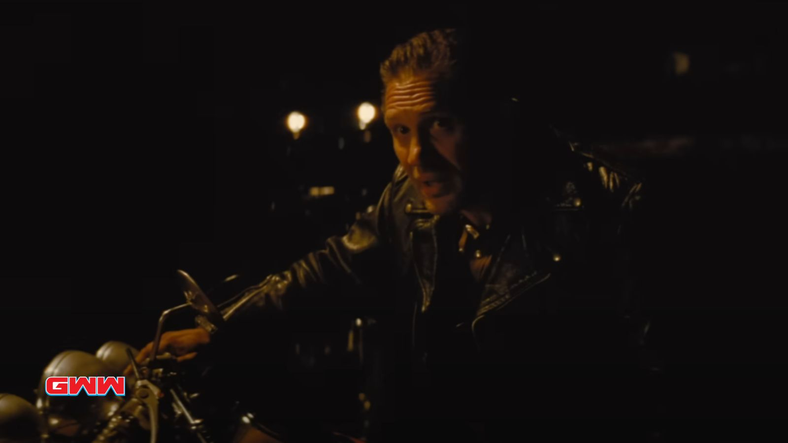 Johnny on a motorcycle at night, wearing a leather jacket, speaking.