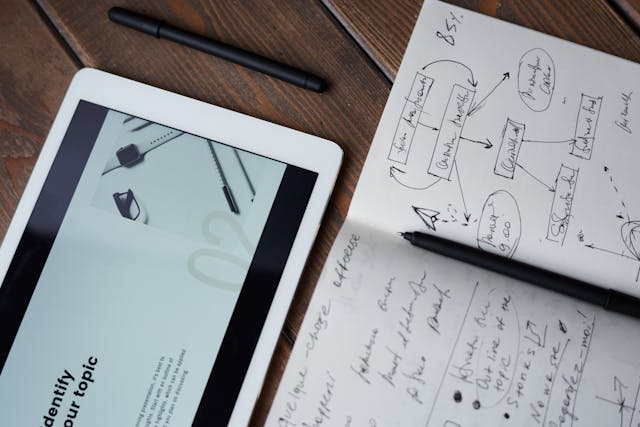 
A tablet and pen on a table with a notebook and pen. Get creative with your ideas and let your imagination flow!