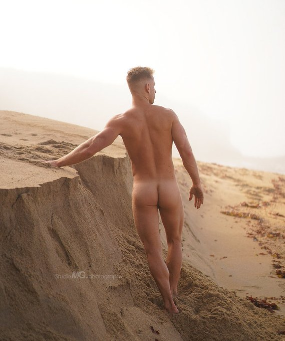 via Studio Mg Photography Sumner Blayne staring off into the ocean on a sand dune naked exposing his ass for the camera