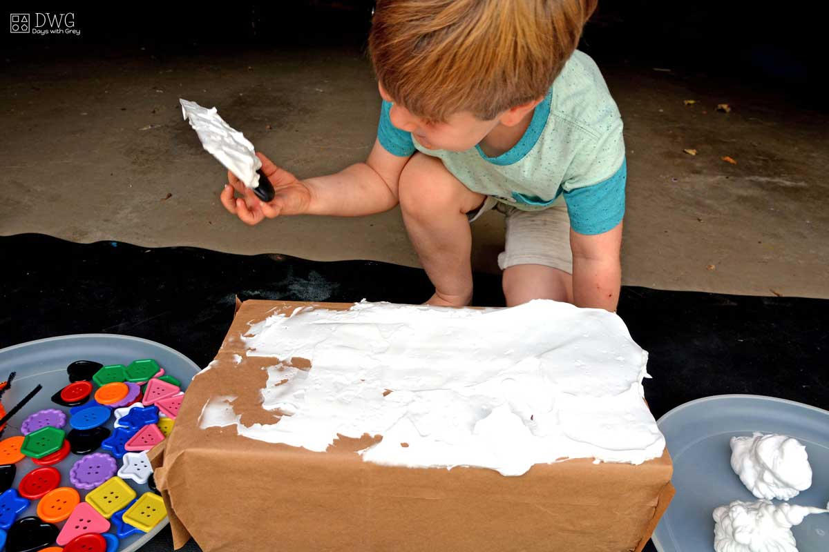 Four-year-old boy is spreading shaving cream on a box to look like a cake.