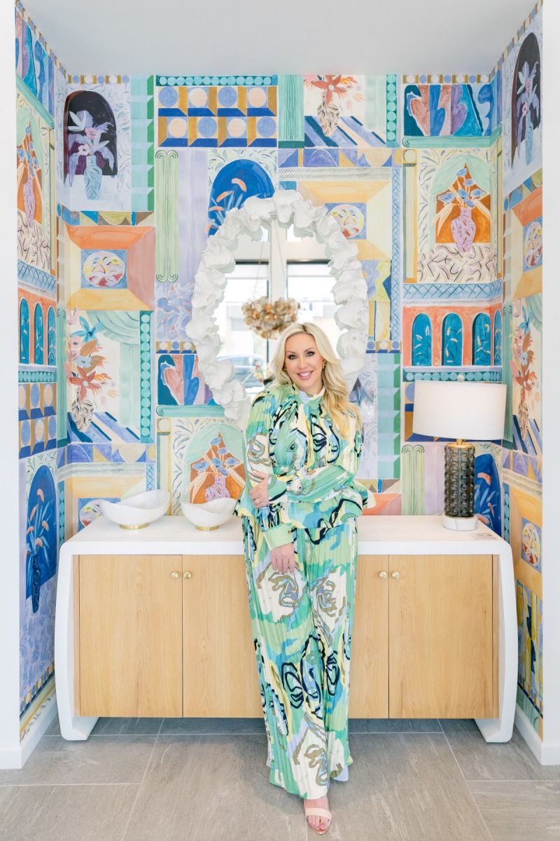 Inside a fully maximized nook, Andrea leans on a modern console table wearing a vividly patterned jumpsuit within a boldly wallpapered space.