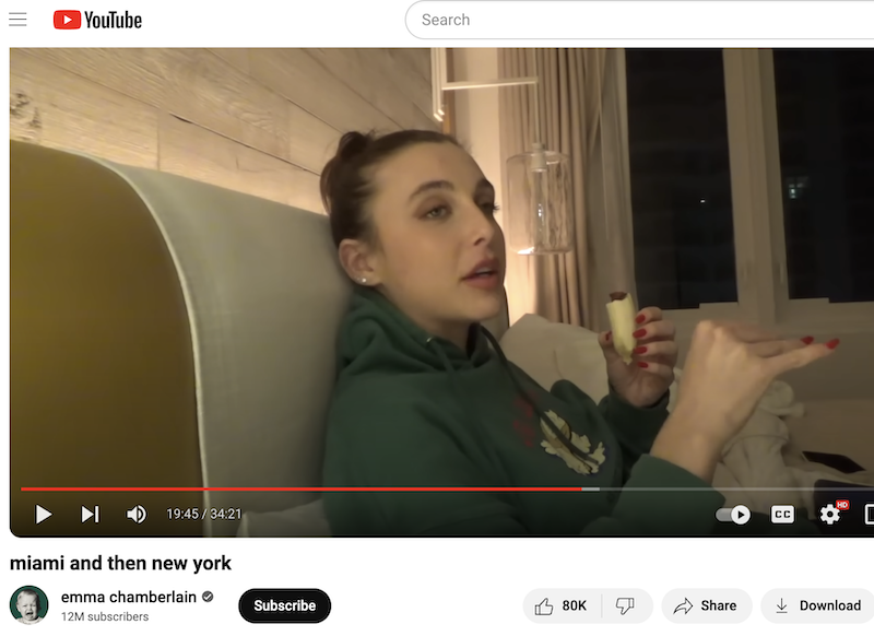 Emma Chamberlain is casually eating what appears to be a banana while millions of people watch her in utter fascination, making her rich.