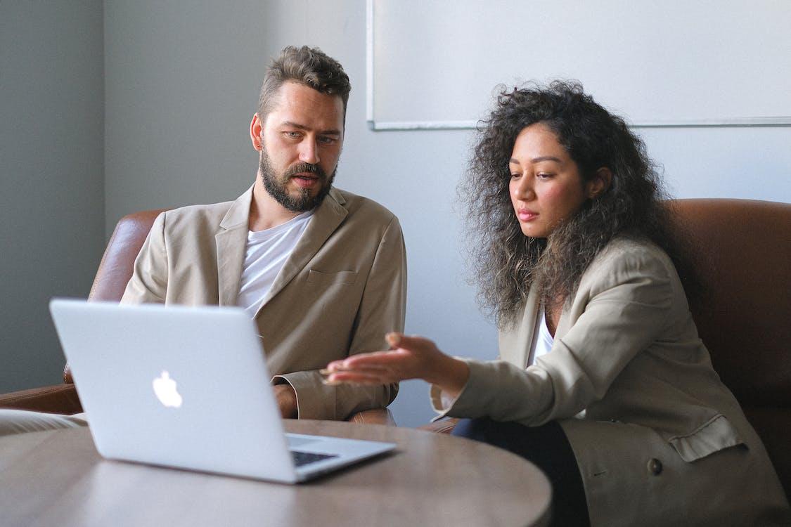 Free Serious colleagues in stylish outfits sitting at table and using laptop while discussing new project in office Stock Photo