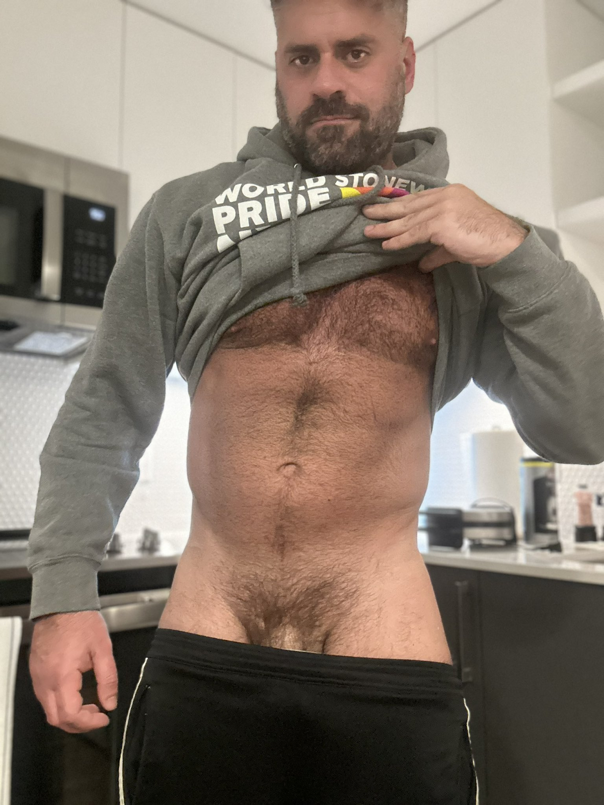 Max Romano lifting up his green hoodie to reveal his flaccid cock and bush and hairy chest and stomach while pulling down his shorts