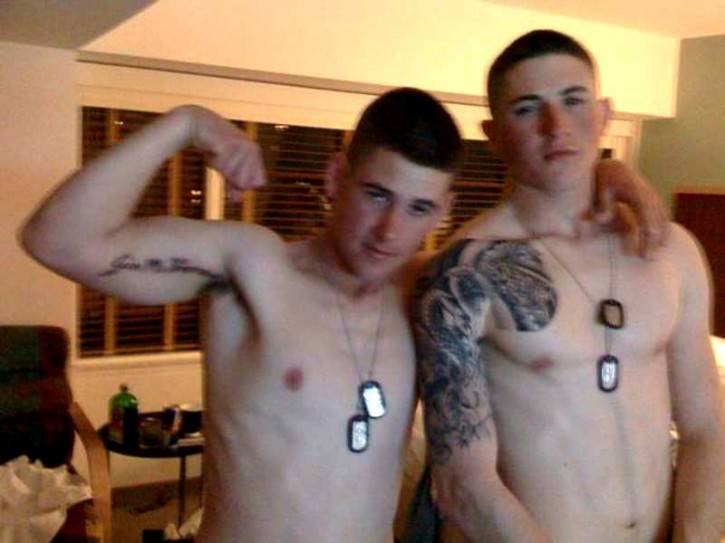 two males with arm tattoos posing together shirtless flexing and wearing army dog tags
