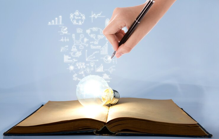 Person drawing symbols coming out of a light bulb atop a book.