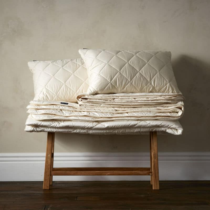 Wool Room duvet folded on wooden bench with two pillows