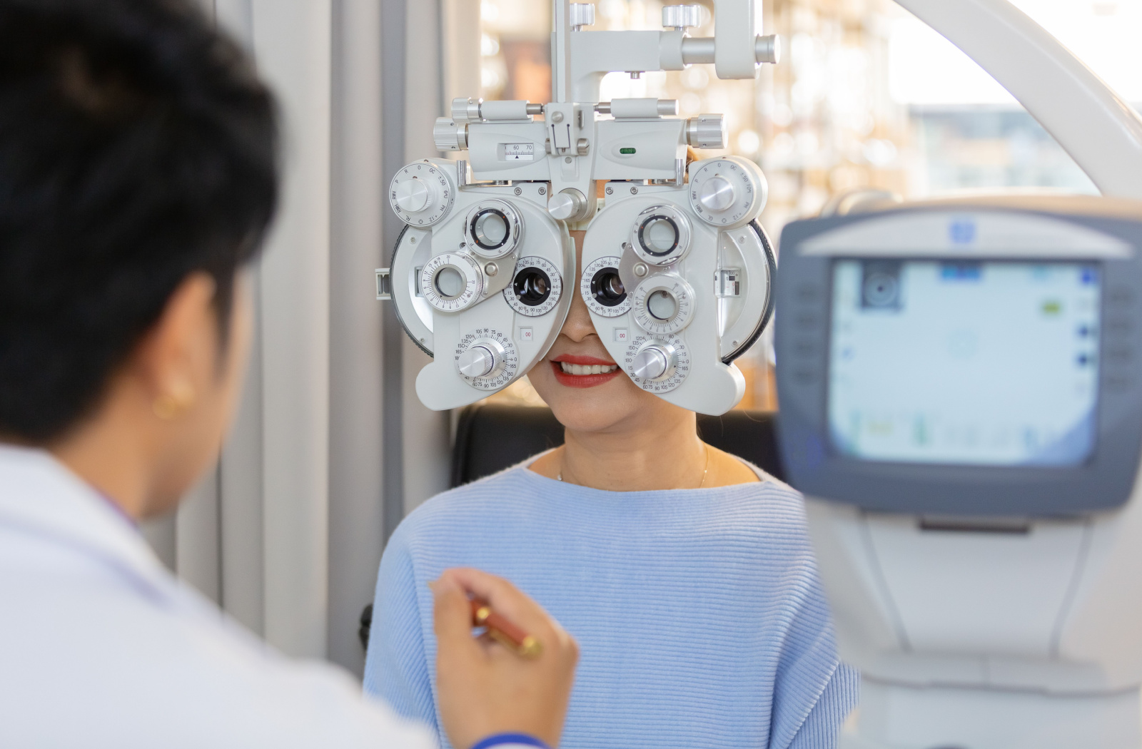 A female patient sitting behind a phoropter at the optometrist's office, and the optometrist is examining her eyes