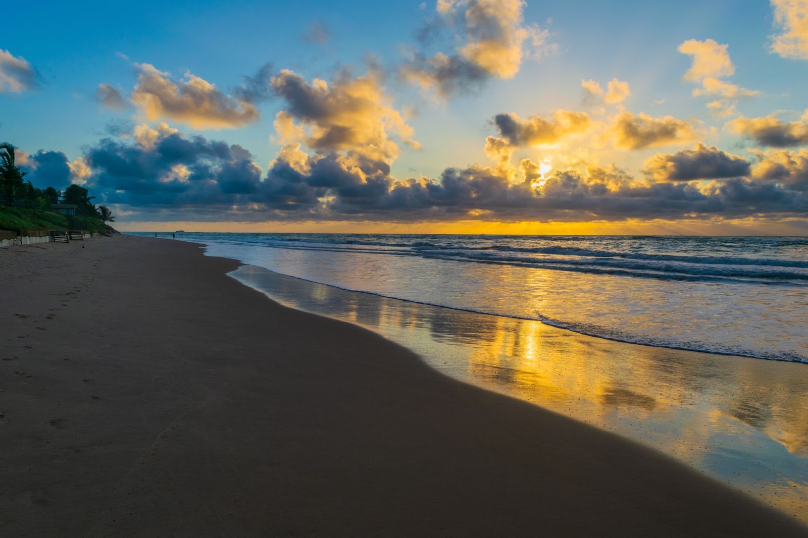 Pôr do sol sobre o mar de Porto de Galinhas, PE. O mar tranquilo reflete o brilho dourado do entardecer. A faixa de areia está limpa e vazia