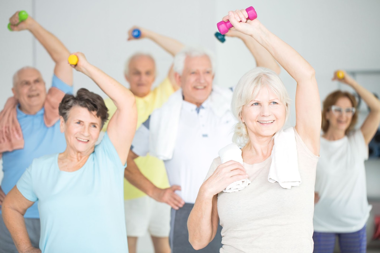 Older adults in a group class smiling and exercising with dumbbells.