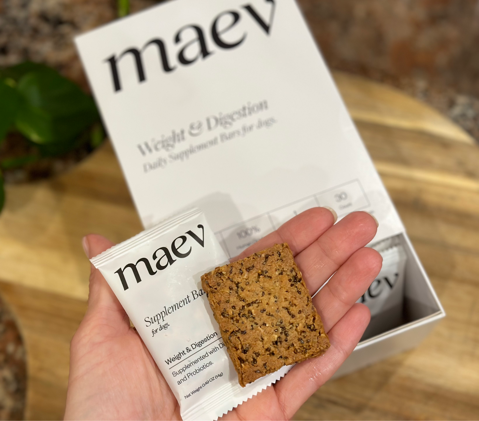 A picture of me holding a Maev supplement bar. They're small squares that resemble a granola bar.