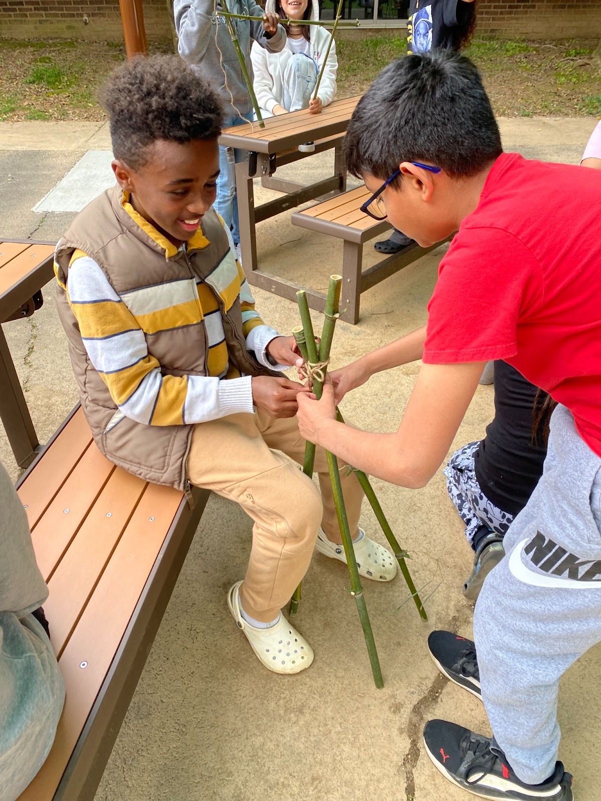 two students work to build a structure out of three bamboo poles