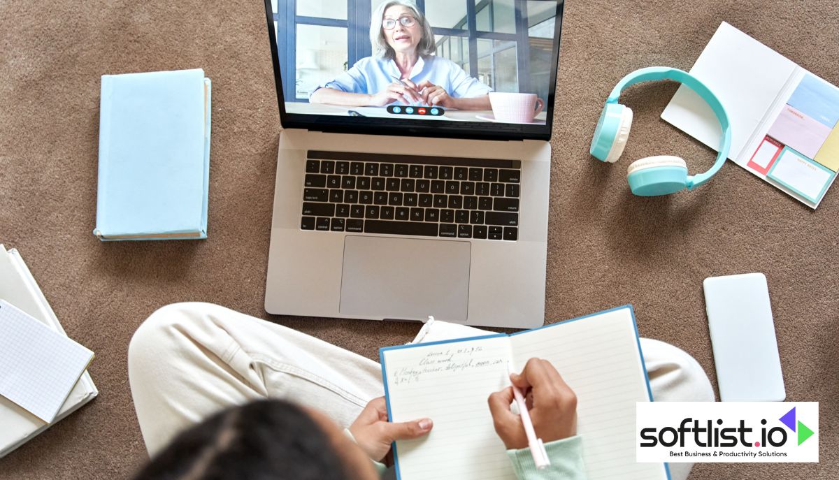 A woman is diligently engaged in an online course, sitting on the floor with a laptop and a notebook by her side.