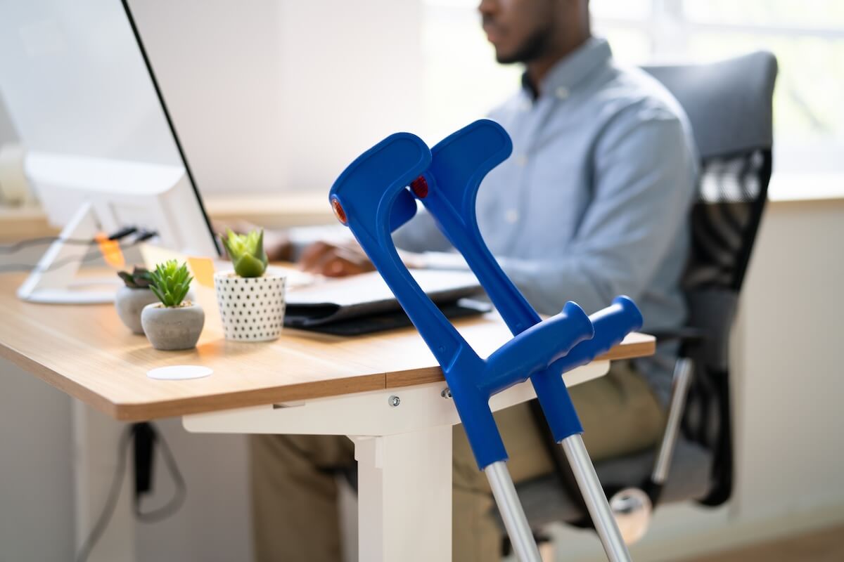 Employee working with his forearm crutches beside his desk