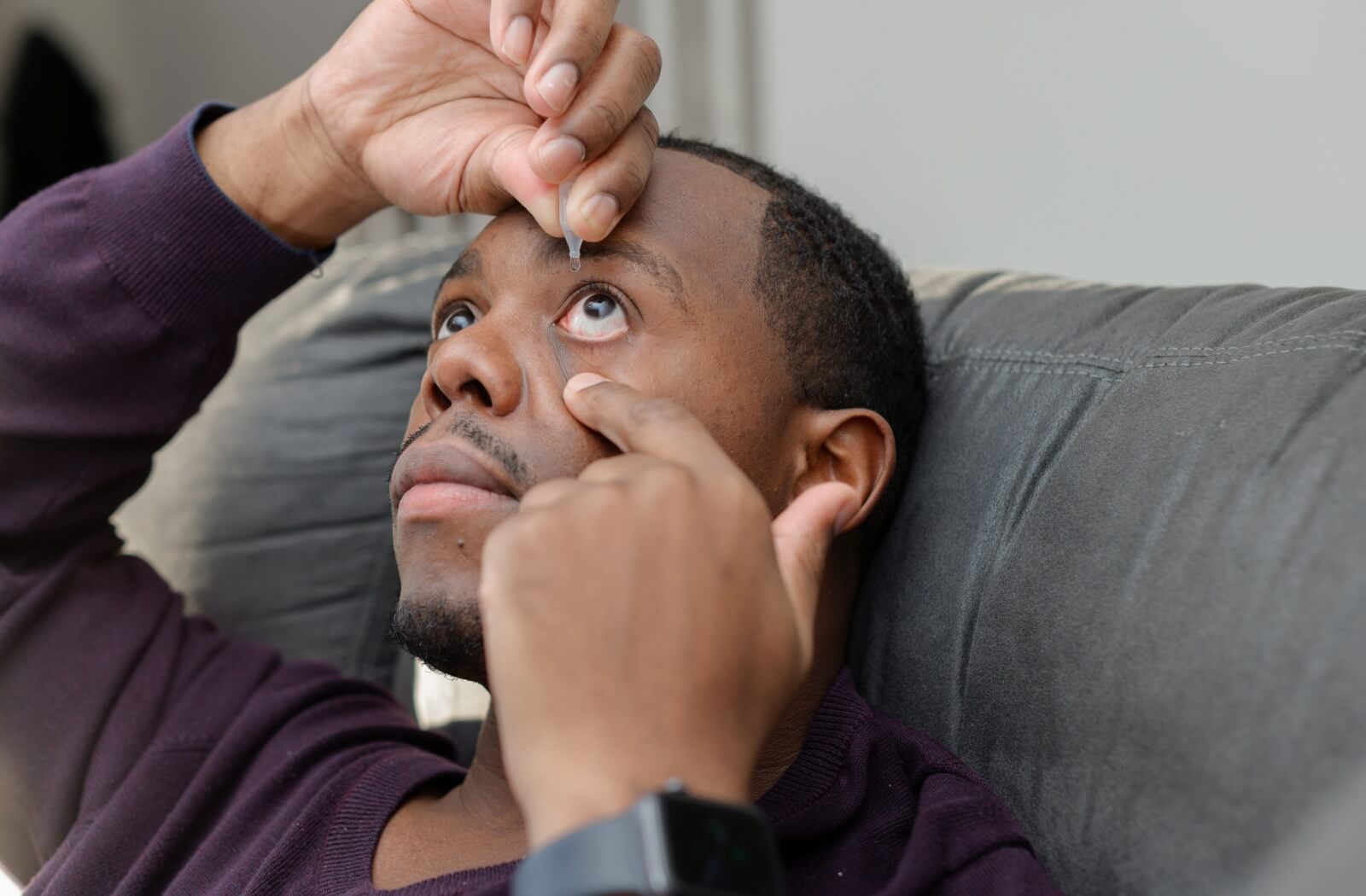 A man pulling his lower eyelid to apply eye drops on his eye.