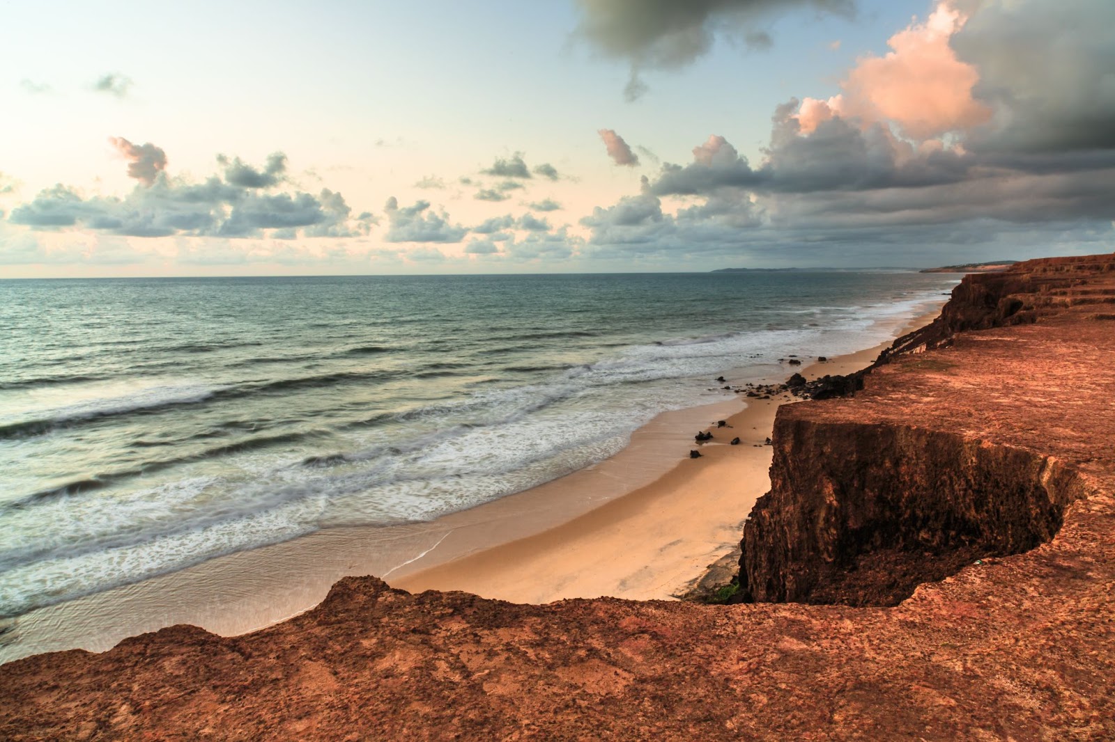 Praia da Pipa vista de cima do chapadão. Mar quase sem ondas em tom de verde escuro com faixa de areia dourada à sua frente.