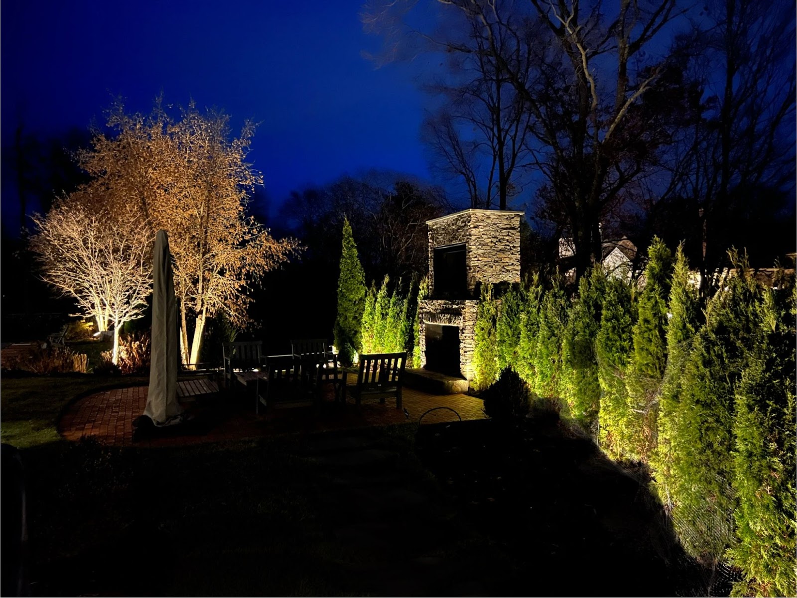 An outdoor gathering space is highlighted by exterior house lighting