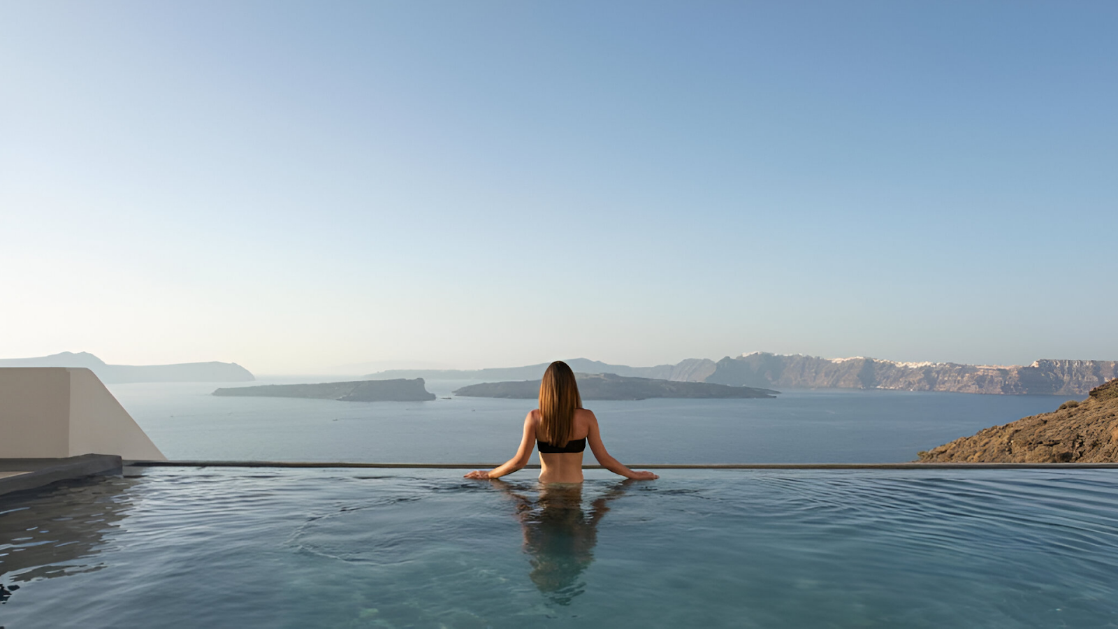 A woman in an infinity pool overlooking the sea in Santorini