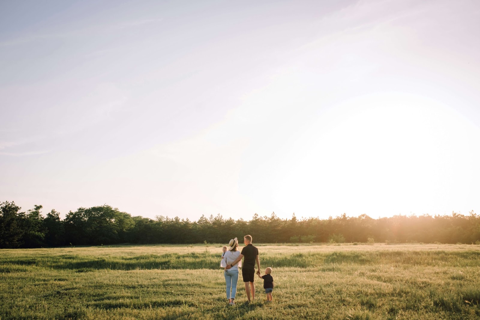 man and woman balancing parenthood while walking with family in a wide open field with sunset in the background.