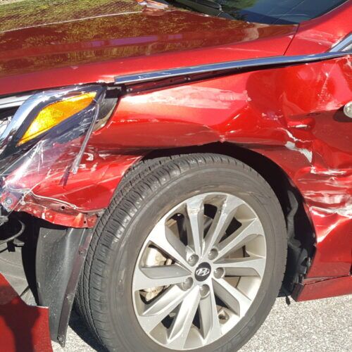 A close-up picture of a red car that has damage to its drivers-side door, the result of car accidents in spring hill