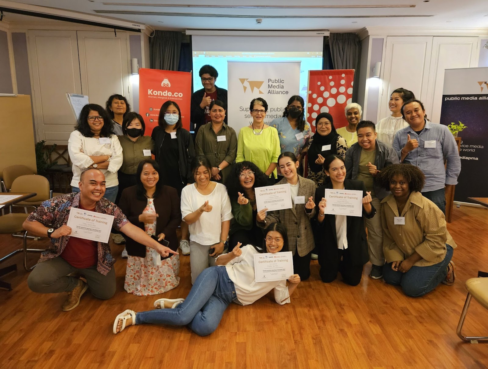 A photo of journalists, media workers, and NGO representatives who participated and facilitated in Public Media Alliance's gender-sensitive reporting workshop. Everyone is smiling, and some are holding up their certificates proudly.