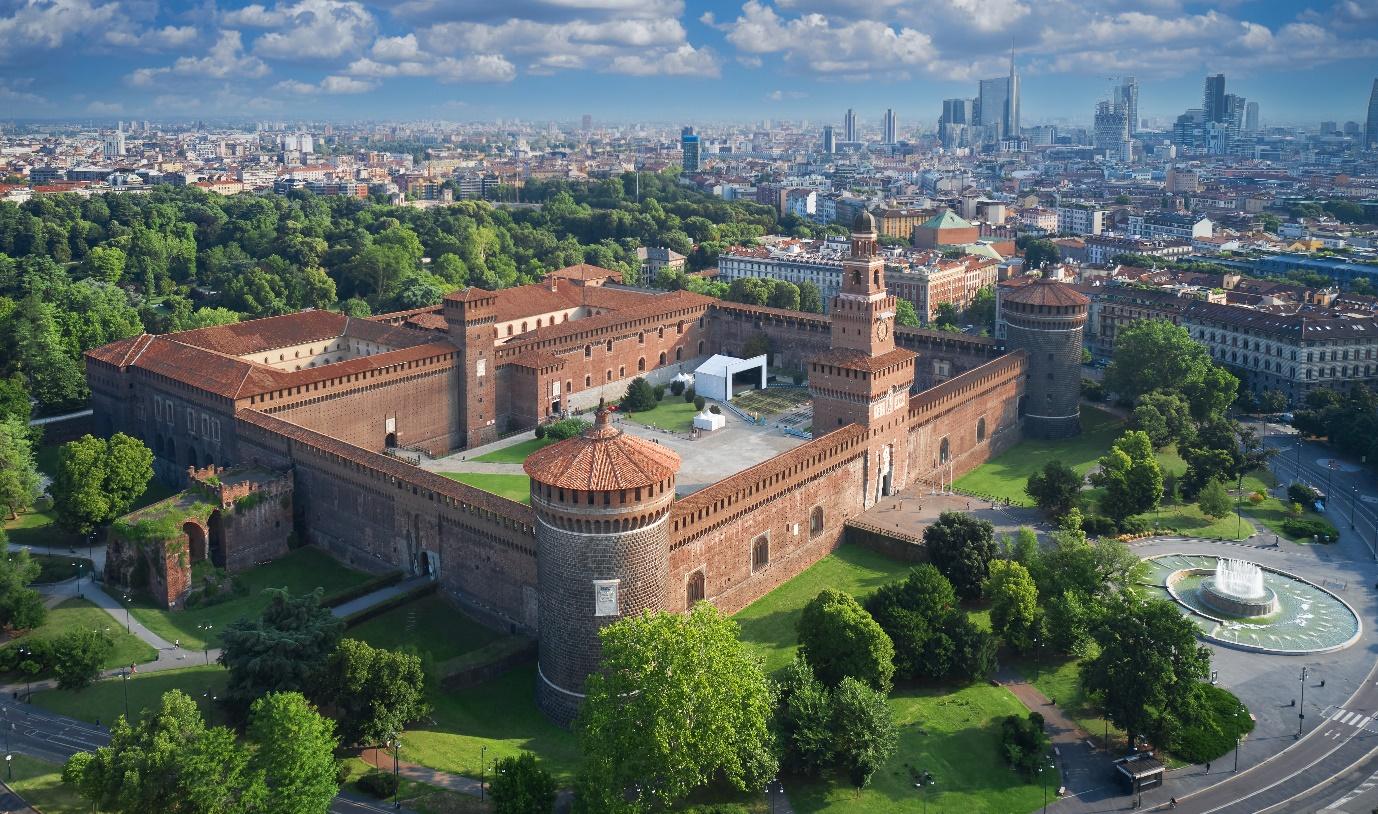 A large brick building with towers and trees in front of it

Description automatically generated