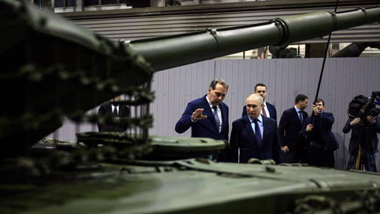 A group of men in suits standing next to a tank

Description automatically generated