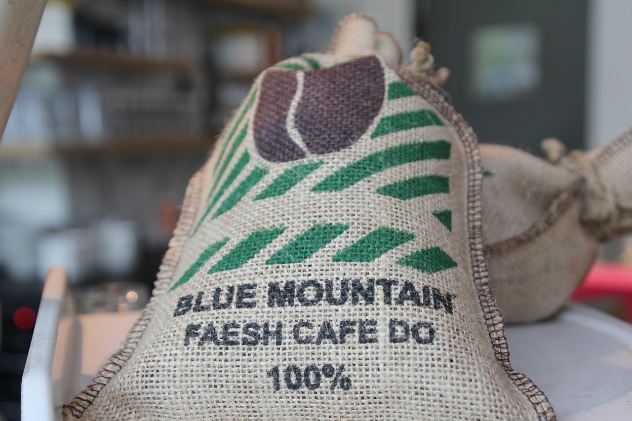 A sack labeled 'Blue Mountain Faesh Café Do 100%' filled with Jamaican coffee beans.